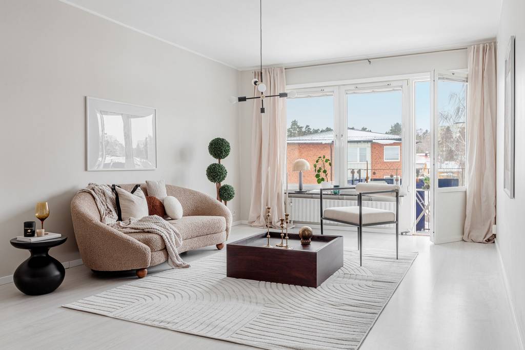 Ljust vardagsrum efter homestyling med beige soffa, stora fönster, ljusa gardiner och minimalistisk inredning.
