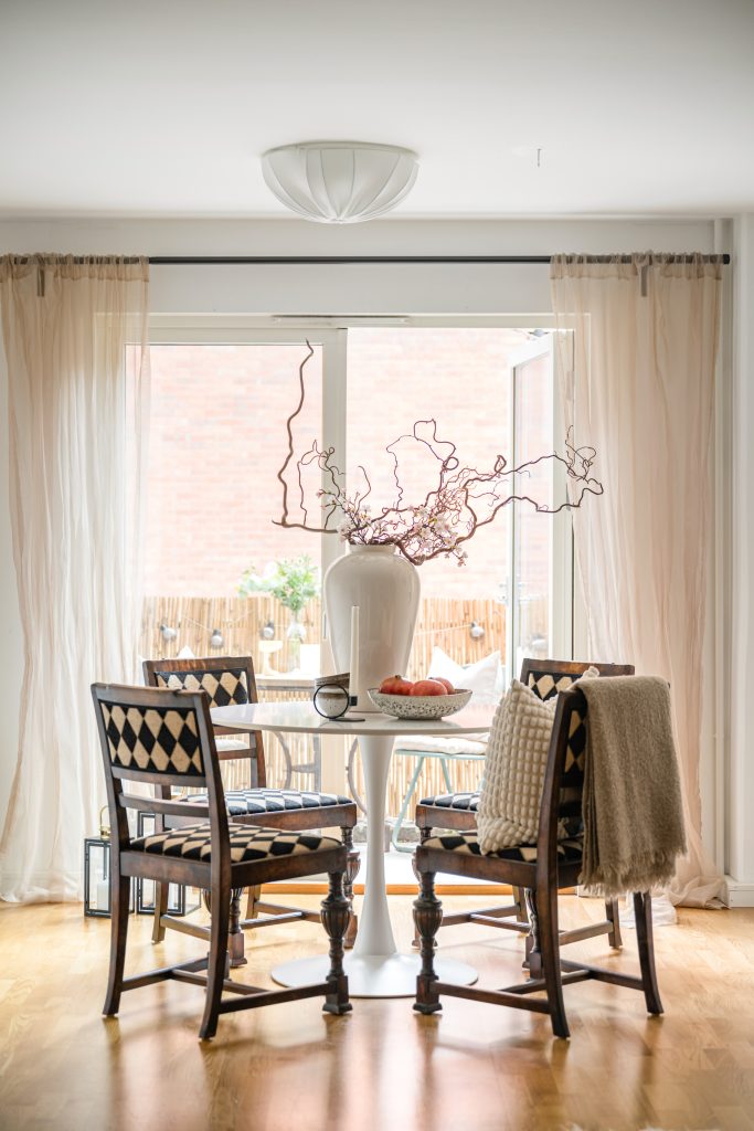 Ljust och öppet matrum efter homestyling med eleganta stolar, rund matplats, stora fönster, blommor och inredningsdetaljer.