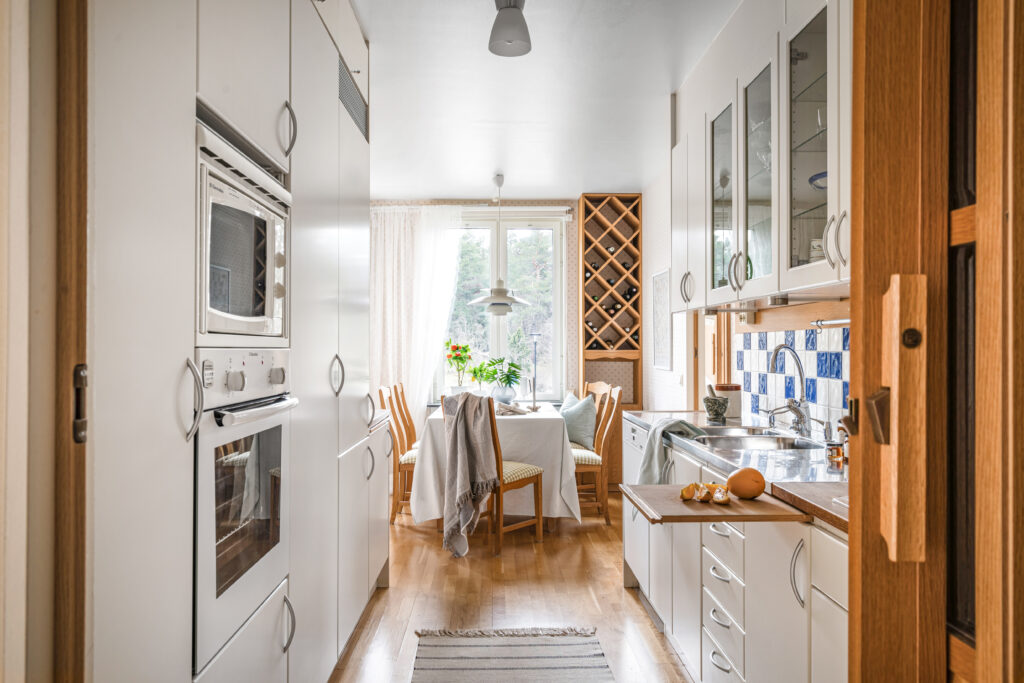 Ljust och stylat kök med trädetaljer, vita skåp, blåvitt kakel och matplats med gröna växter efter homestyling