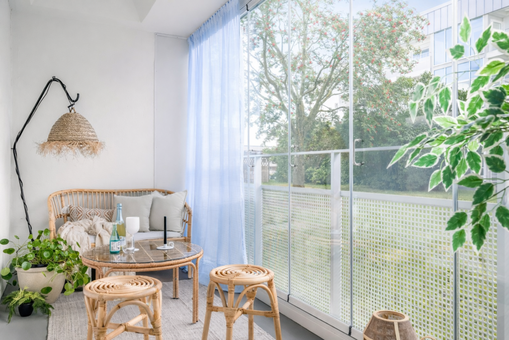 Ljus veranda efter homestyling med glasväggar, gröna växter och rottingpallar i modern stil.