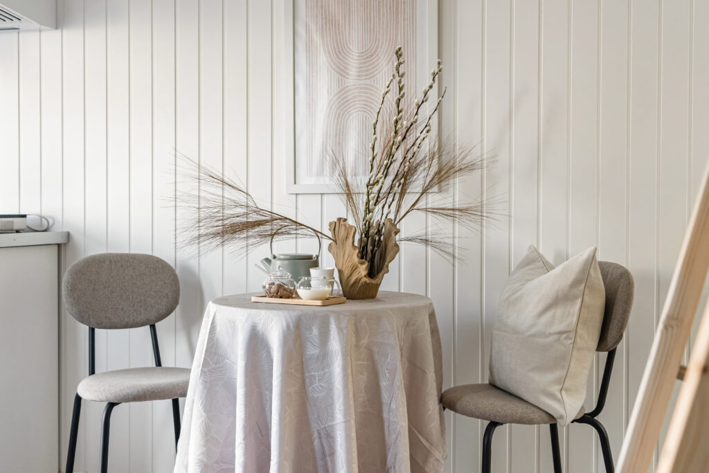 Liten rund matplats med två stolar, beige duk, dekorativ vas med torkade grenar och keramik, i ljus skandinavisk stil.