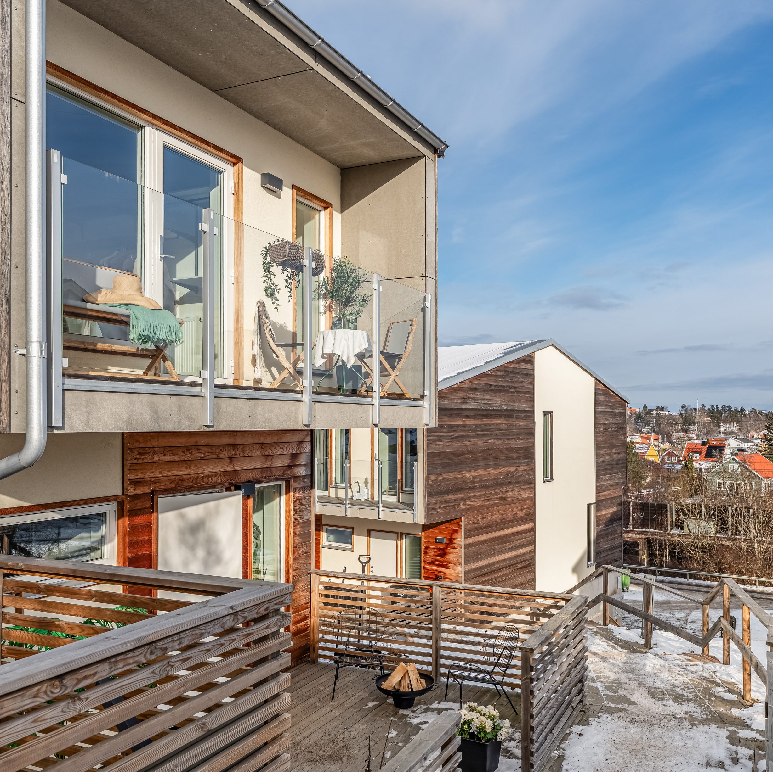 Modern balkong och uteplats efter homestyling med glasräcke, sittgrupp, grönskande växter och utsikt över villaområde i vintermiljö.