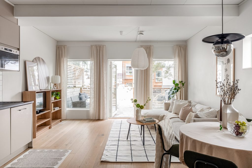 Ljust vardagsrum efter homestyling med stora fönster, beige soffa, gröna växter och matplats i öppen planlösning.